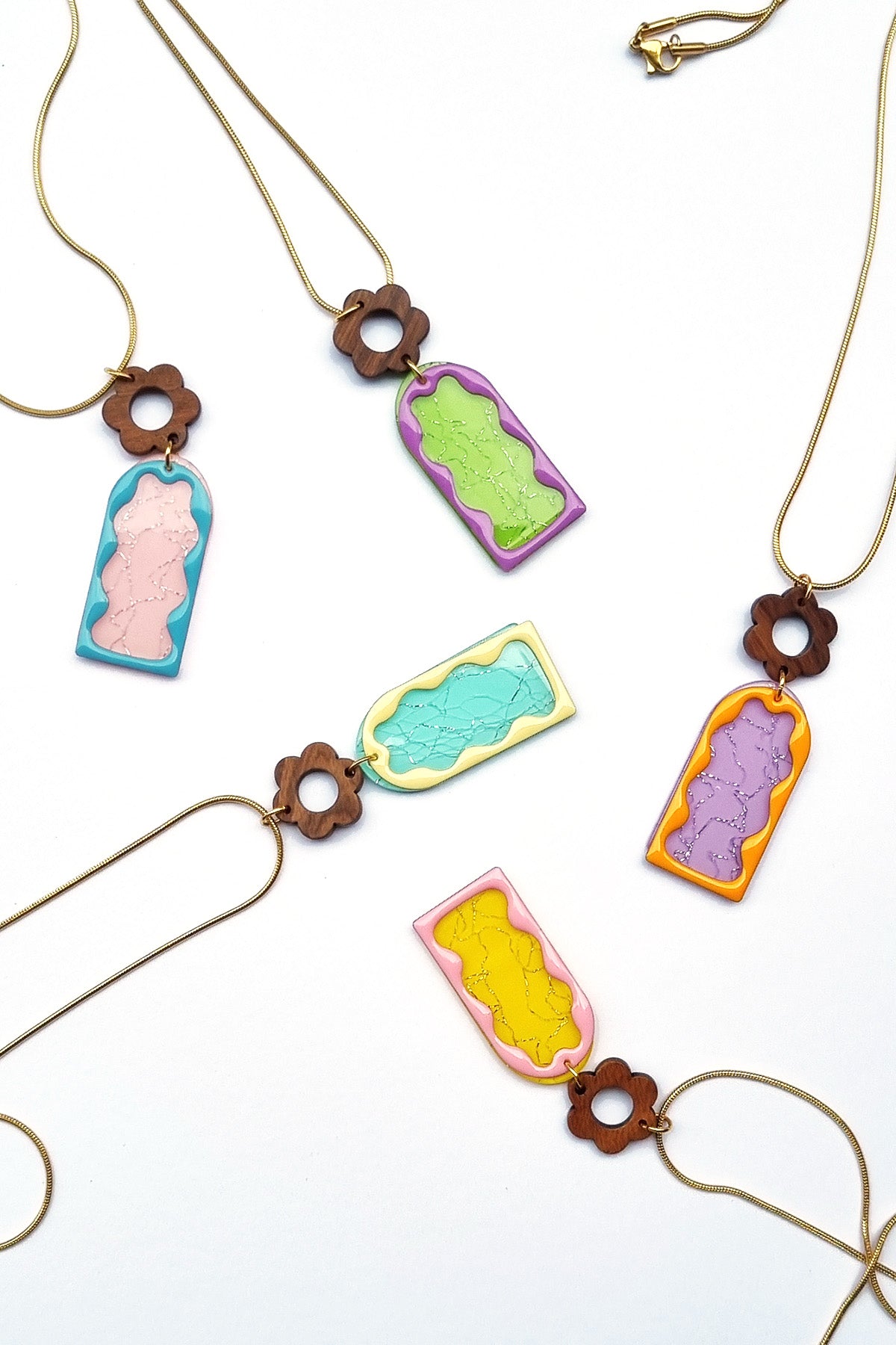 Four mixtape necklaces in the five colourways; Purple with orange frame, Aqua with yellow frame, Yellow with pink frame,  Green with purple frame, and Pink with blue frame lay flat against a white background.