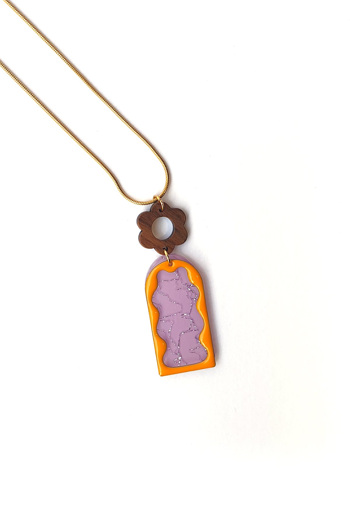 A necklace lays against a white background. It features a gold chain, a wooden flower top, followed by a purple acrylic arch with silver thread detail overlaid by an orange acrylic wavy arch frame. 