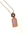 A necklace lays against a white background. It features a gold chain, a wooden flower top, followed by a purple acrylic arch with silver thread detail overlaid by an orange acrylic wavy arch frame. 