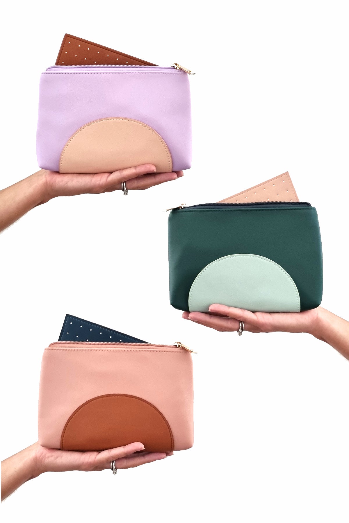 Three outstretched hands hold three Cartwheel purses against a white background. The purses are lilac with a peach half circle and tan insert, forest green with a duckegg half circle and peach insert, and pink with a tan half circle and teal insert.