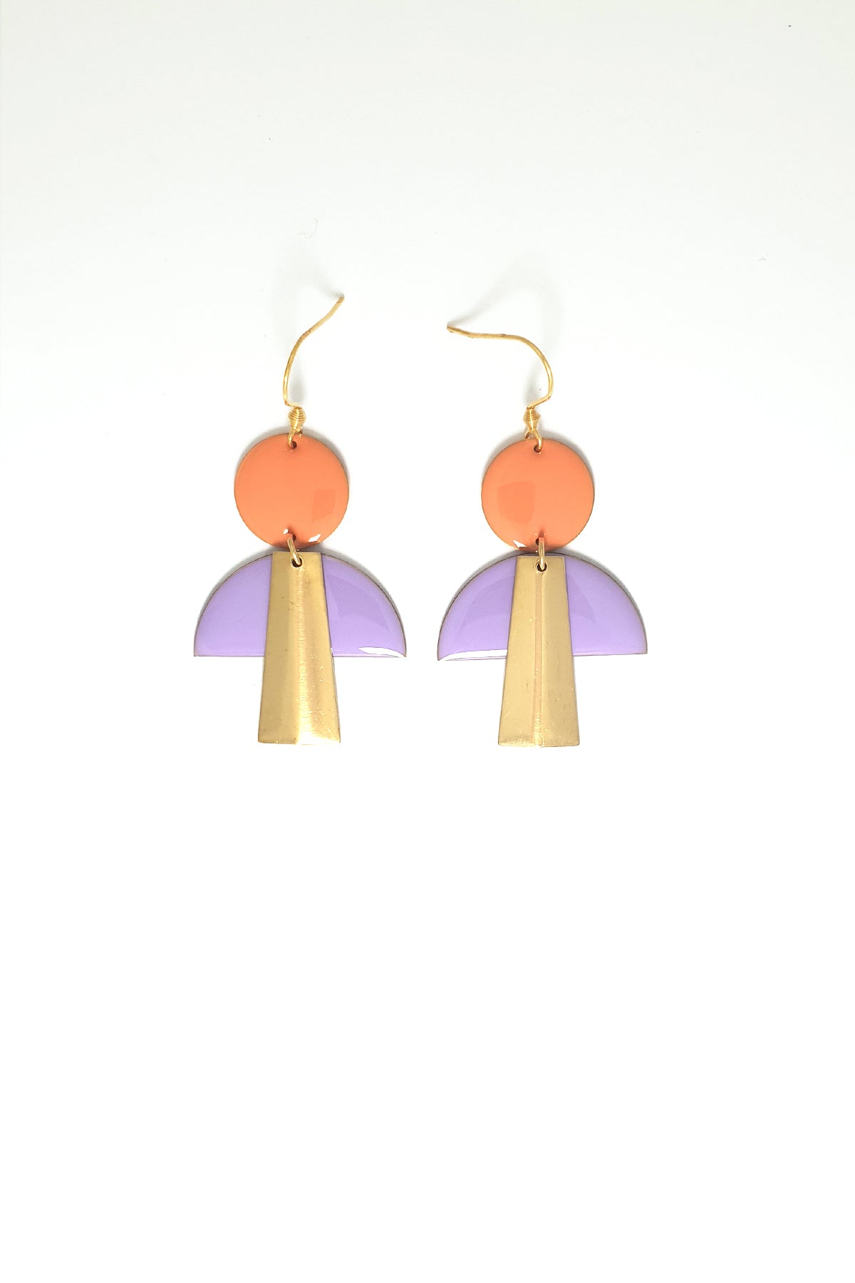 A pair of hook dangle earrings are placed against a white background. They feature a peach enamel dot, a lilac enamel arch shape, and an elongated trapezoid brass piece.