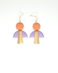 A pair of hook dangle earrings are placed against a white background. They feature a peach enamel dot, a lilac enamel arch shape, and an elongated trapezoid brass piece.