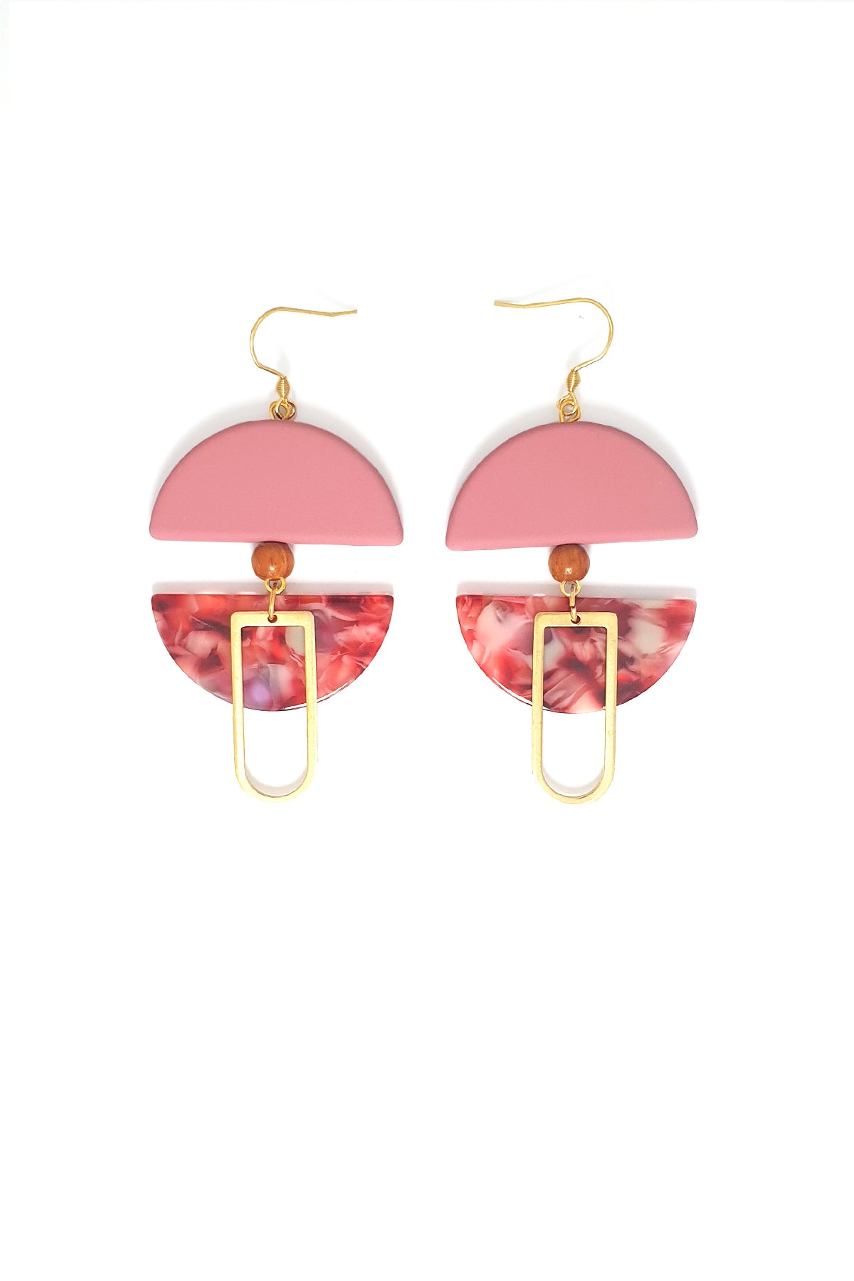 A pair of dangle earrings with a hook sit against a white background. They feature a pink arch shaped bead, a small wooden bead, a pink acrylic half circle, and an elongated D shape brass piece.