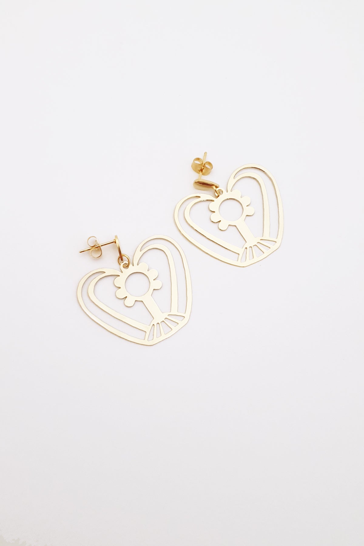 A pair of statement gold plated brass earrings sit angled against a white background. They feature a small gold stud top, and a custom brass geometric shape that resembles a lady with curly hair with her arms above her head in the shape of a heart.
