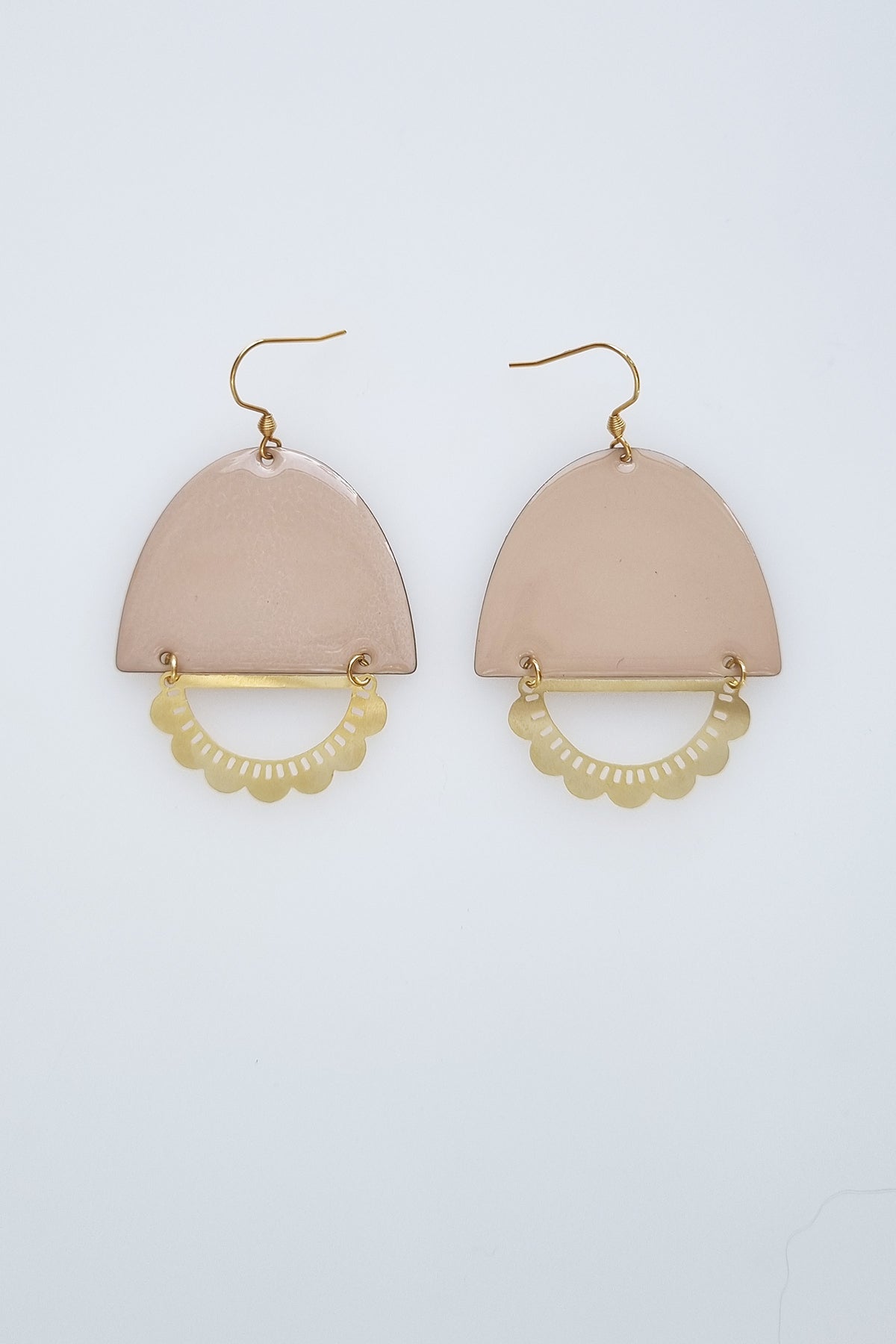 A pair of statement earrings with a hook sit against a white background. They feature a macadamia enamel arch and a horizontal plated brass D shape with scalloped detail.