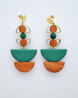 A pair of statement stud dangle earrings sit against a white background. They feature a small brass arch with a round wooden bead inside the arch, followed by a green bead, another small brass arch upturned with a wooden circle bead inside, followed by a green D shape bead, and wooden a D shape bead. 
