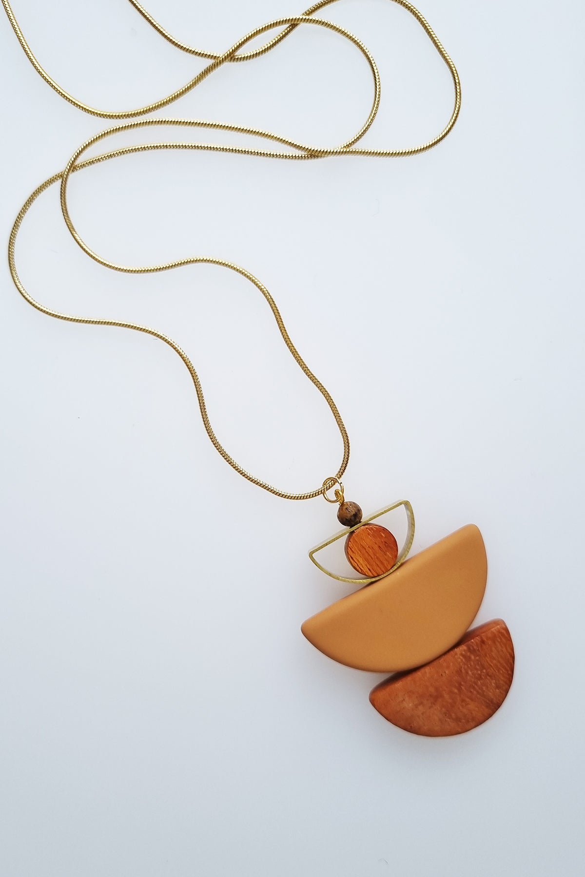 A necklace with a gold chain sits against a white background. It features a small wooden bead, followed by a brass D shape with a wooden circle bead enclosed, followed by a mustard D shaped bead, and a wooden D shape bead.