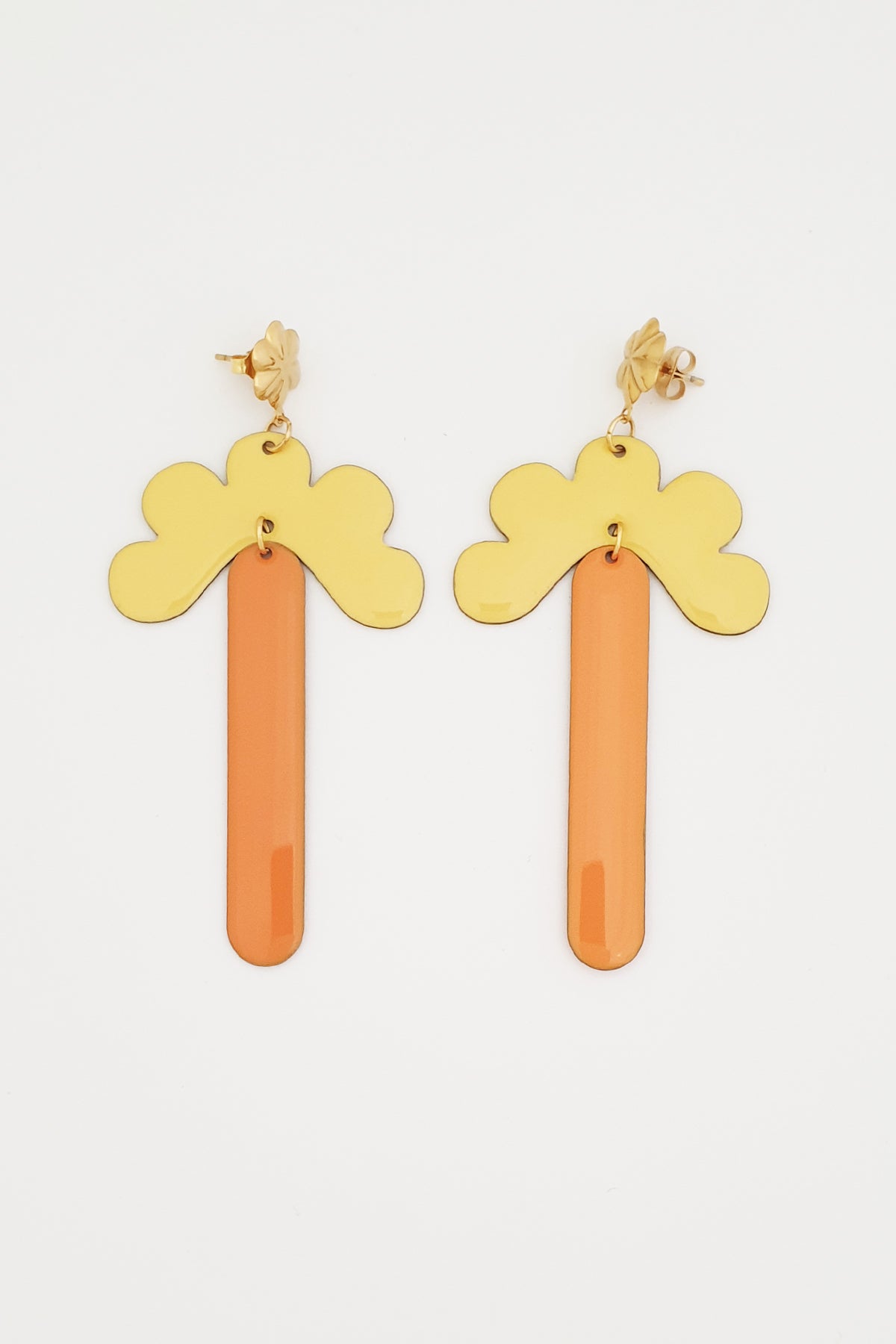 A pair of stud dangle earrings lay against a white background. They feature a gold flower shaped stud top, a yellow enamel connector piece with resemblance to a half flower, and an orange enamel drop.
