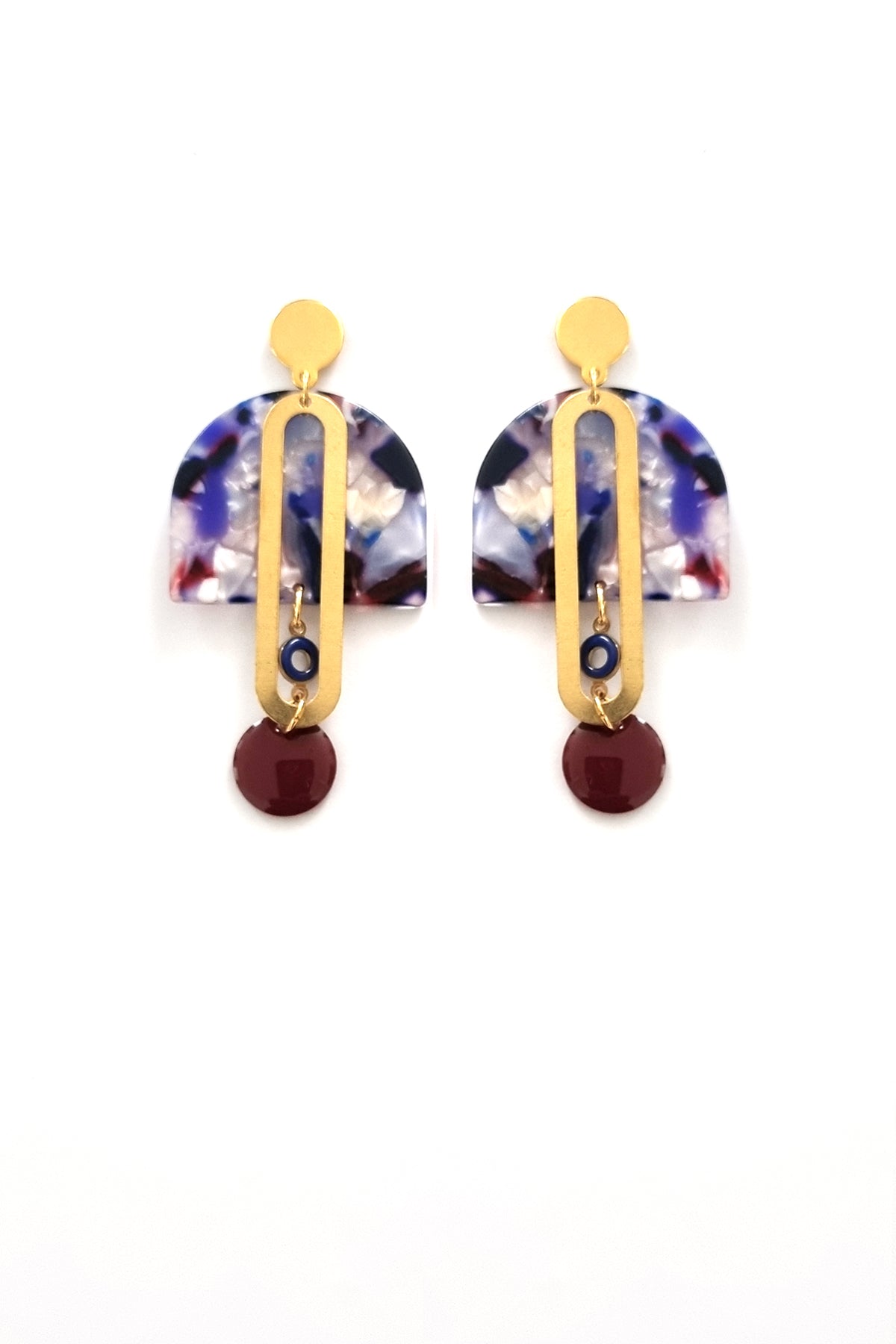A pair of stud dangle earrings sits against a white background. They feature a blue multicoloured acrylic arch, an elongated oval brass piece with a small blue enamel connector attaching the acrylic piece to the brass, and at the bottom hangs a bordo red enamel dot.